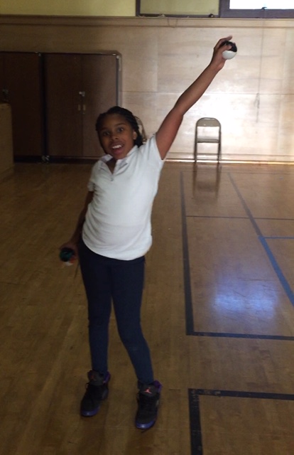 school age girl smiling and holding her left arm up and right arm down, styling with juggling bean bags in her hands
