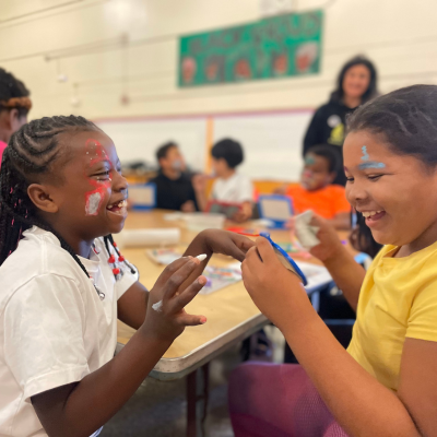 Two Prescott Circus students laughing while helping eachother with their costume makeup.